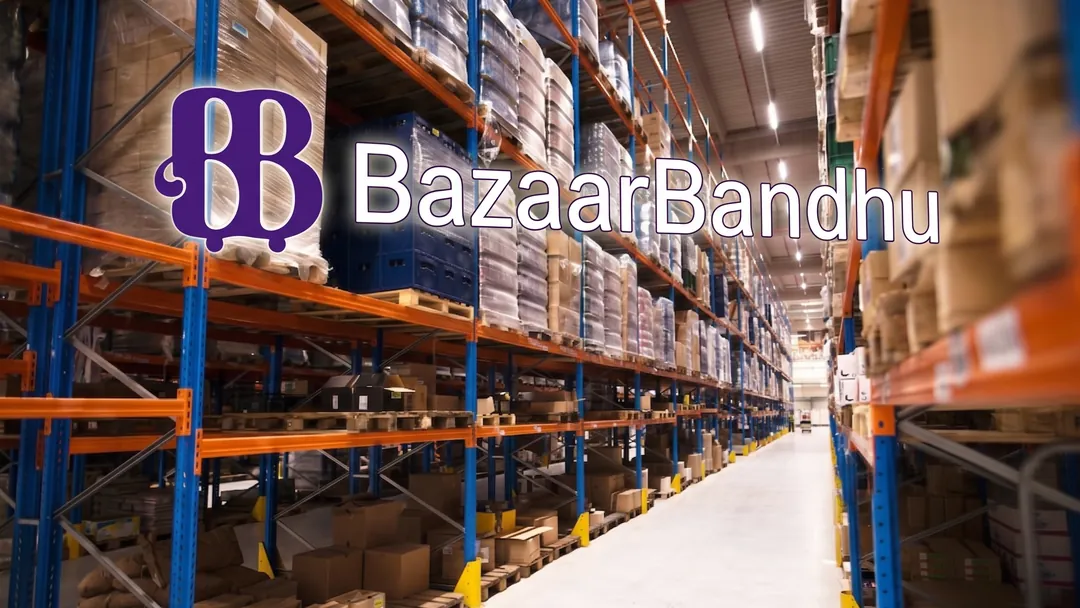 The BazaarBandhu wordmark over the aisle of a wholesale distribution warehouse, pallet racking stacked high on both sides